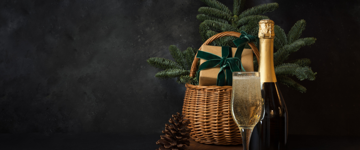 a bottle of champagne with a basket filled with ever green branches against a grey background